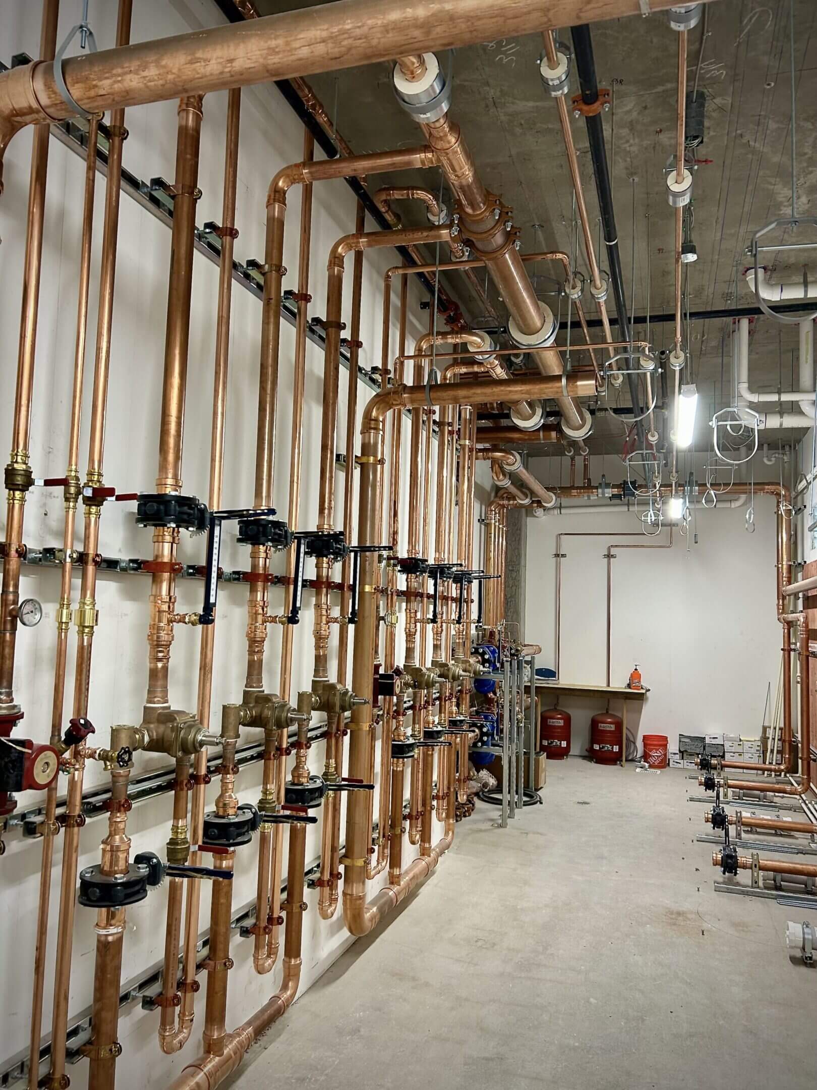 Industrial pipes and valves installed along a concrete wall in a utility room.