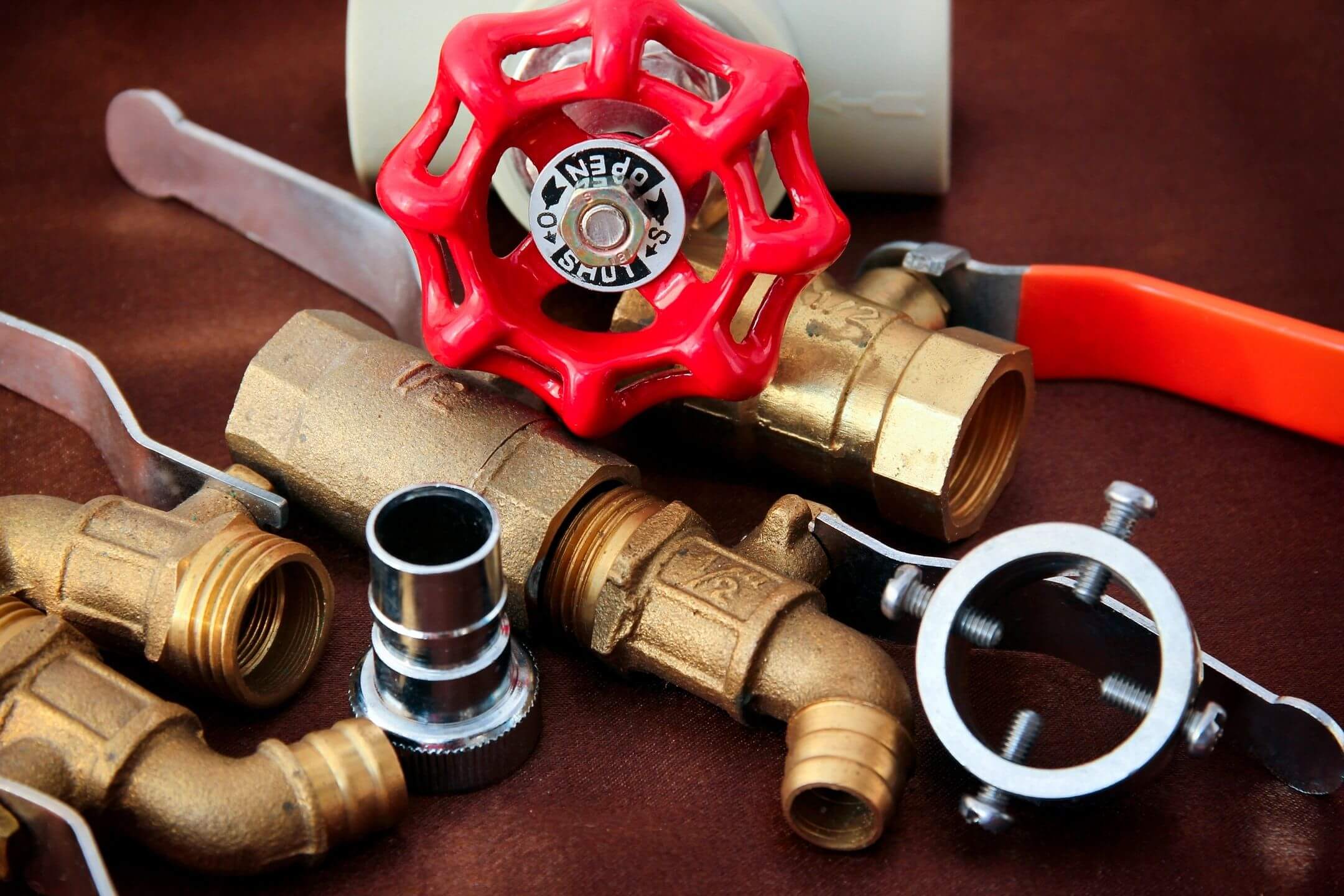 Close-up of plumbing tools and brass fittings with a red valve handle.